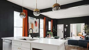 A modern kitchen with a central island, white cabinetry, and a black backsplash. - Indy Getaway - Near Downtown Indy - Sleeps 10! (Indianapolis)