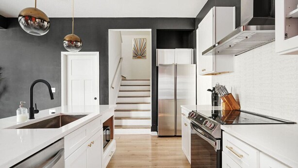 A modern kitchen with white cabinetry, a stainless steel refrigerator, a built-in oven, and a black faucet. - Indy Getaway - Near Downtown Indy - Sleeps 10! (Indianapolis)