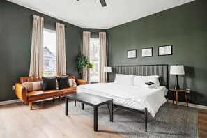 A bedroom with a bed, a sofa, a bedside table, a lamp, and a window with curtains. - Indy Getaway - Near Downtown Indy - Sleeps 10! (Indianapolis)