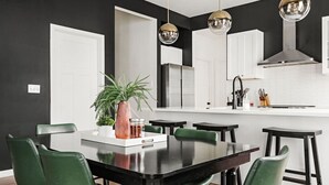 A modern kitchen with a central island, pendant lighting, and a dining area with green chairs. - Indy Getaway - Near Downtown Indy - Sleeps 10! (Indianapolis)