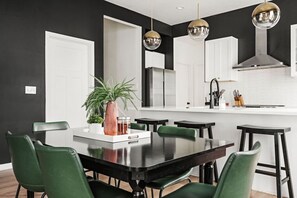 A modern kitchen with a central island, pendant lighting, and a dining area with green chairs. - Indy Getaway - Near Downtown Indy - Sleeps 10! (Indianapolis)