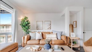 Een moderne woonkamer met een leren bank, een salontafel en een groot raam met uitzicht op een gebouw.