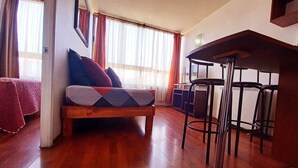 Una habitación acogedora con piso de madera, un sofá con cojines estampados, una mesa de comedor con sillas y un taburete de bar.