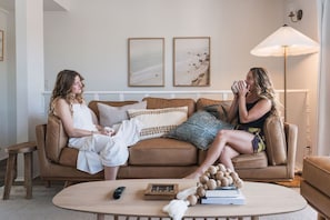 Ein Wohnzimmer mit einem braunen Ledersofa, einem runden Couchtisch mit Büchern und einer Fernbedienung sowie einer Stehlampe.
