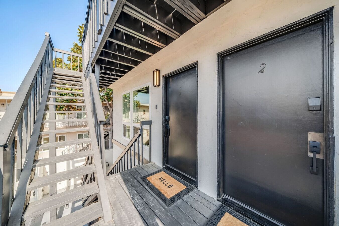 A modern building with a metal staircase, a black door with a number, and a welcome mat.
