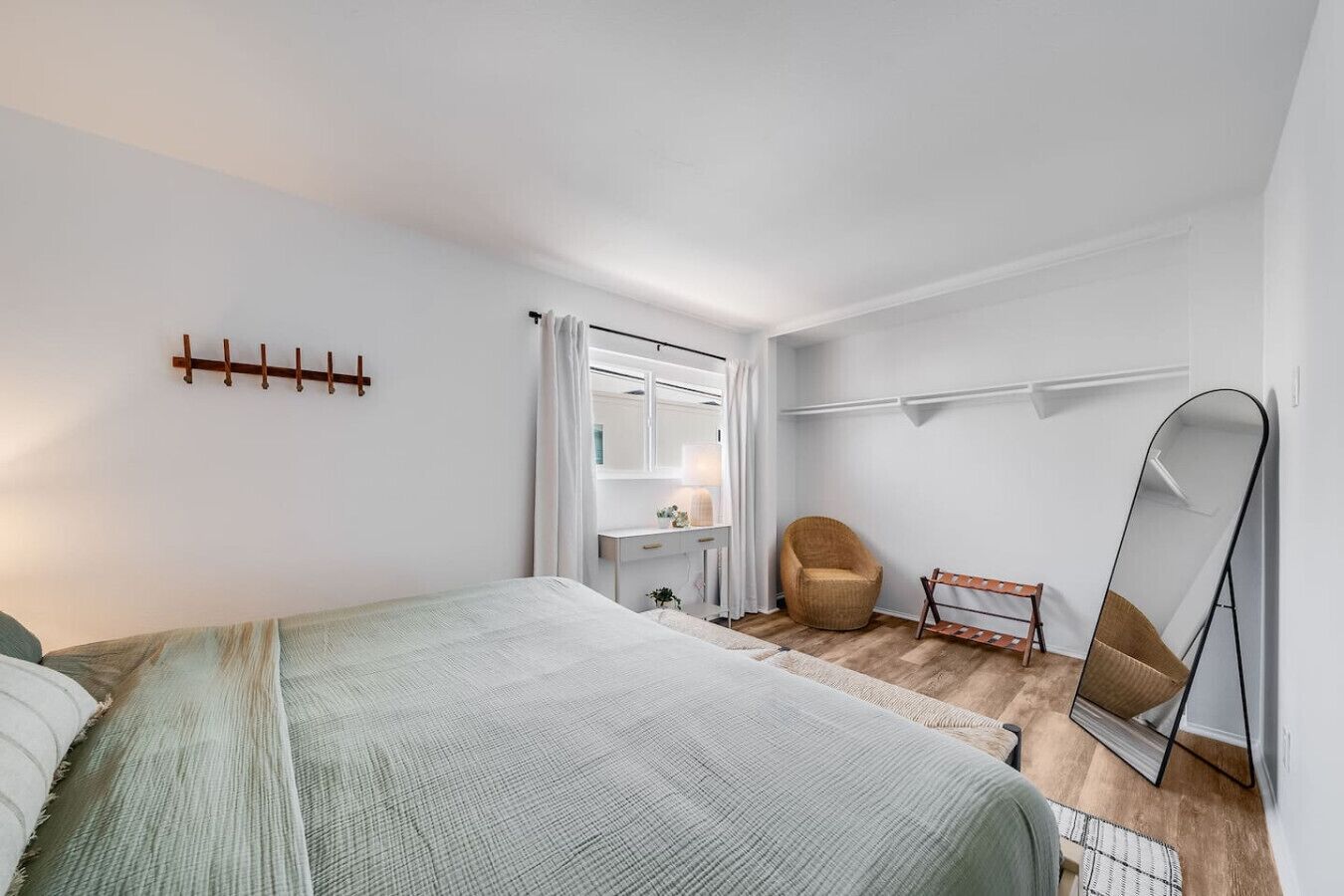 Un dormitorio con cama, una silla, escritorio, espejo y perchero.