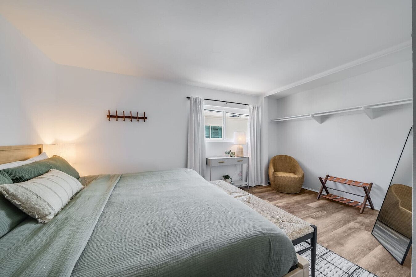 Ein Schlafzimmer mit einem Bett, einem Nachttisch, einem Stuhl, einem Schreibtisch, einem Spiegel und einem Kleiderschrank.