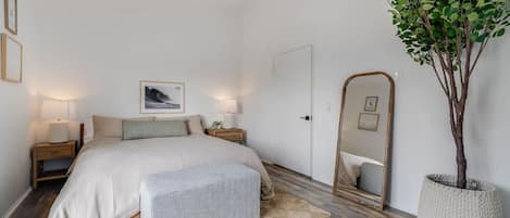 Une chambre à coucher avec un lit, des tables de chevet, un miroir, une plante en pot et une porte.