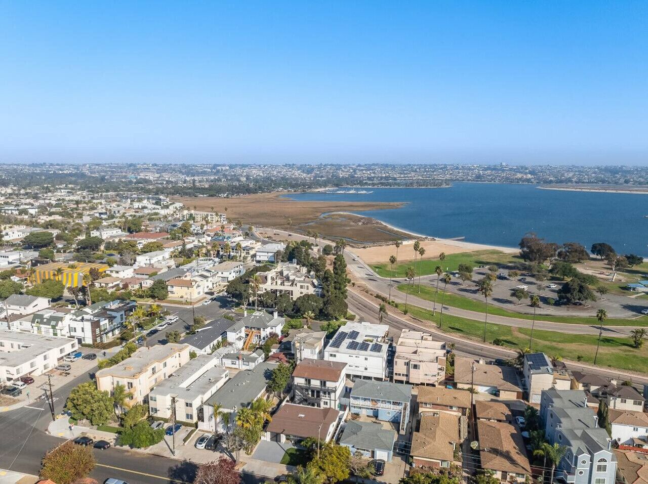 An aerial view of a coastal town with residential buildings, a beach, and a clear blue sky.