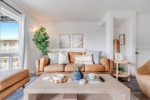 A modern living room with a leather sofa, a coffee table, and a large window with a view of a building. - Pacific Beach Escape with Central AC & King Beds! (San Diego)