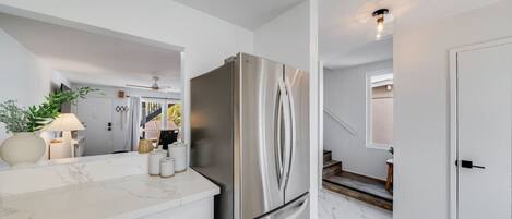 A modern kitchen with a stainless steel refrigerator, white cabinetry, and a marble countertop.