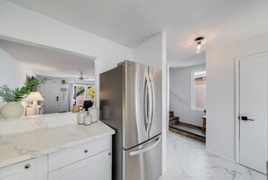 A modern kitchen with a stainless steel refrigerator, white cabinetry, and a marble countertop. - Pacific Beach Escape with Central AC & King Beds! (San Diego)