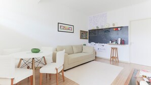 A modern living room with a white sofa, dining table, and chairs, a chalkboard wall with writing, and a small stool. - Fully furnished apartment near Higienópolis Shopping Mall. (São Paulo)