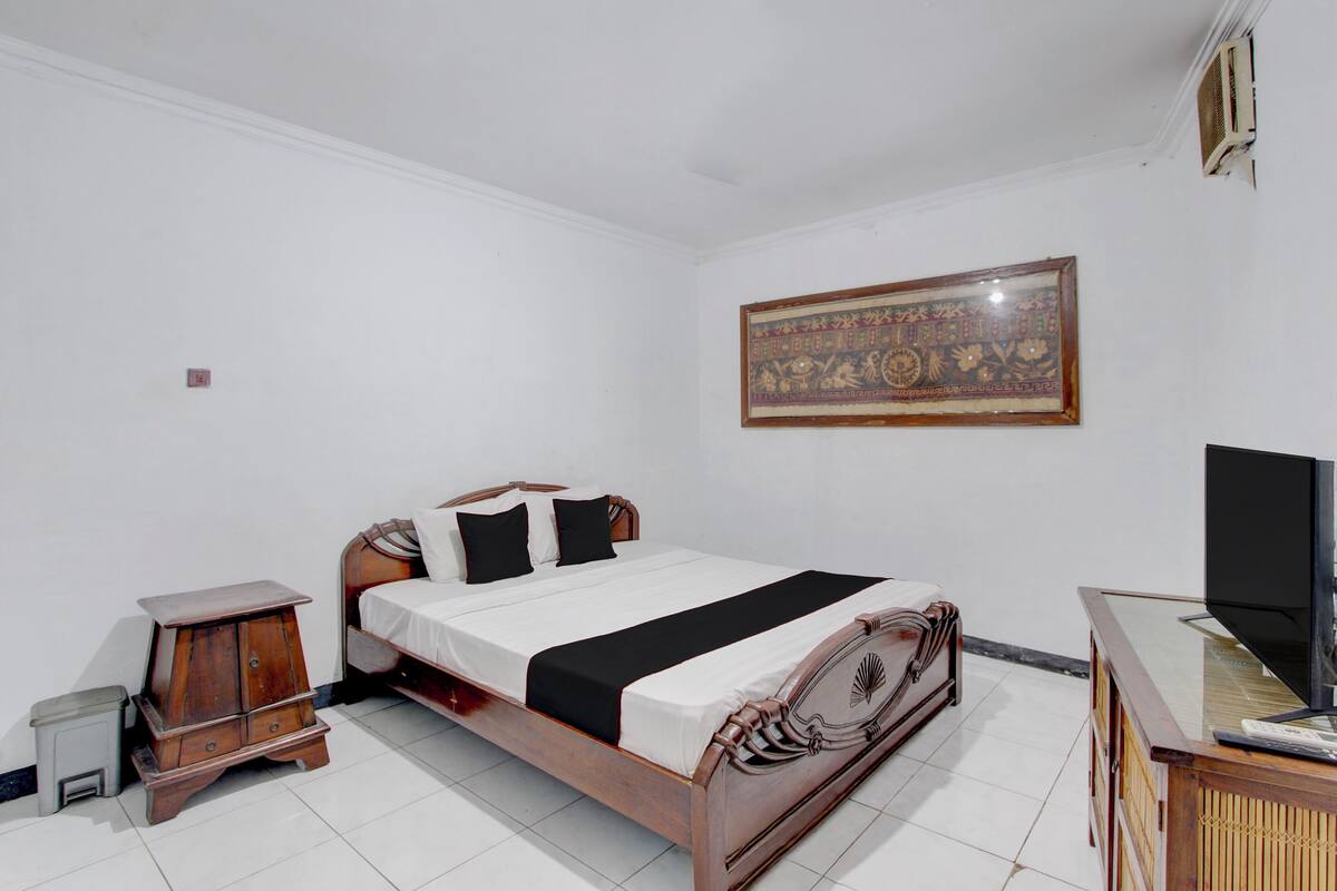 A bedroom with a bed, a wooden nightstand, a television, and a decorative wall hanging.