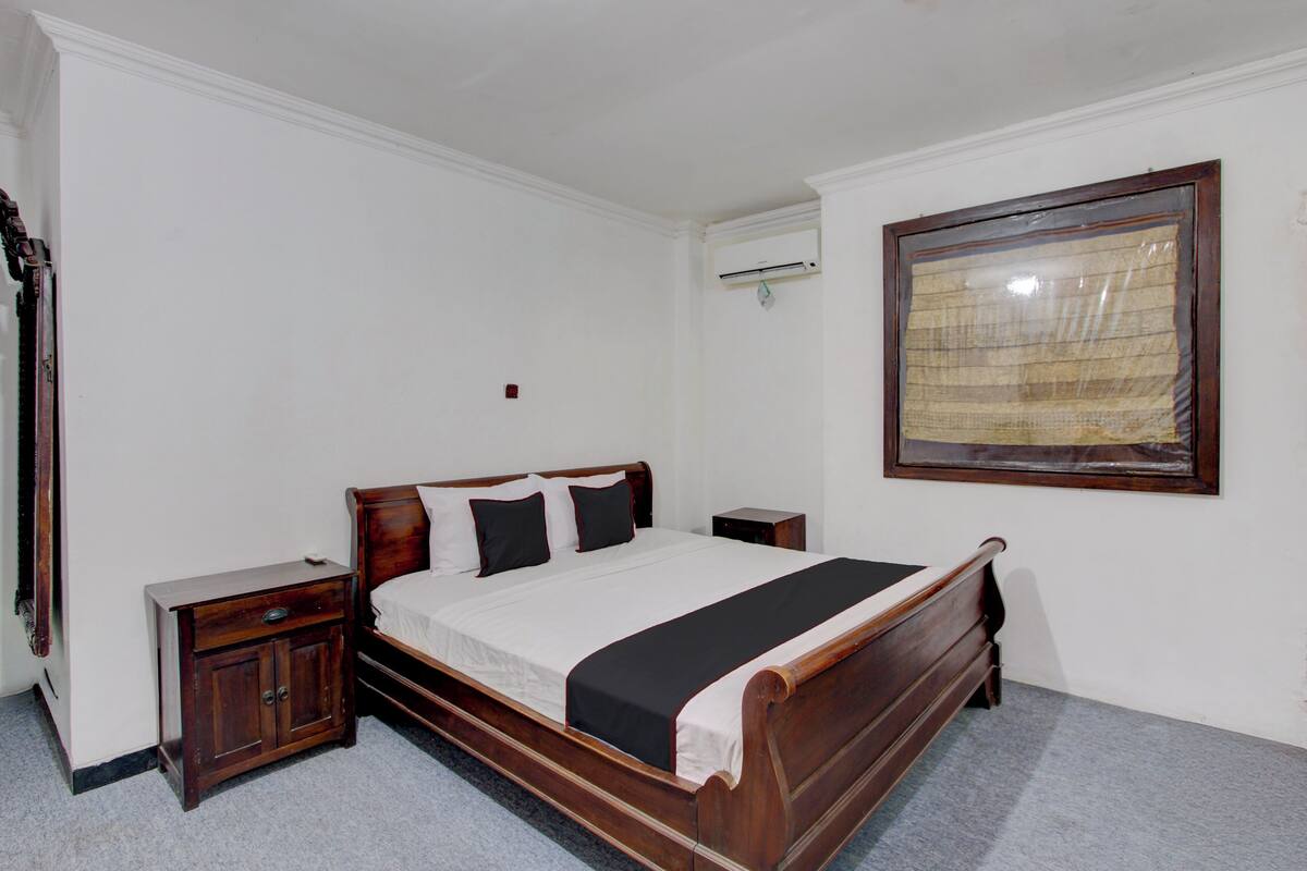 A bedroom with a wooden bed, a nightstand, a dresser, a wall-mounted air conditioner, and a framed picture.