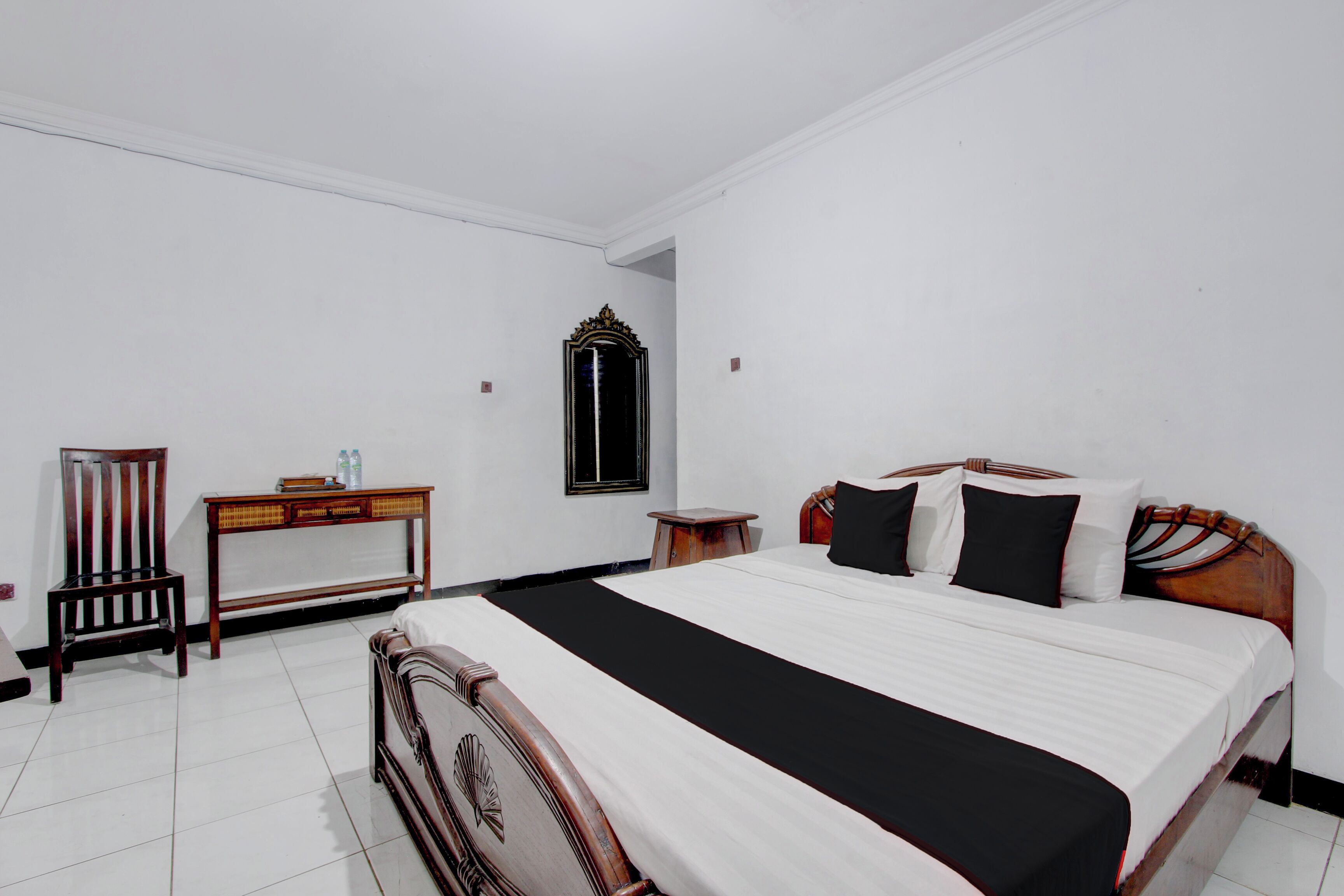 A bedroom with a bed, a chair, a small table, and a mirror.