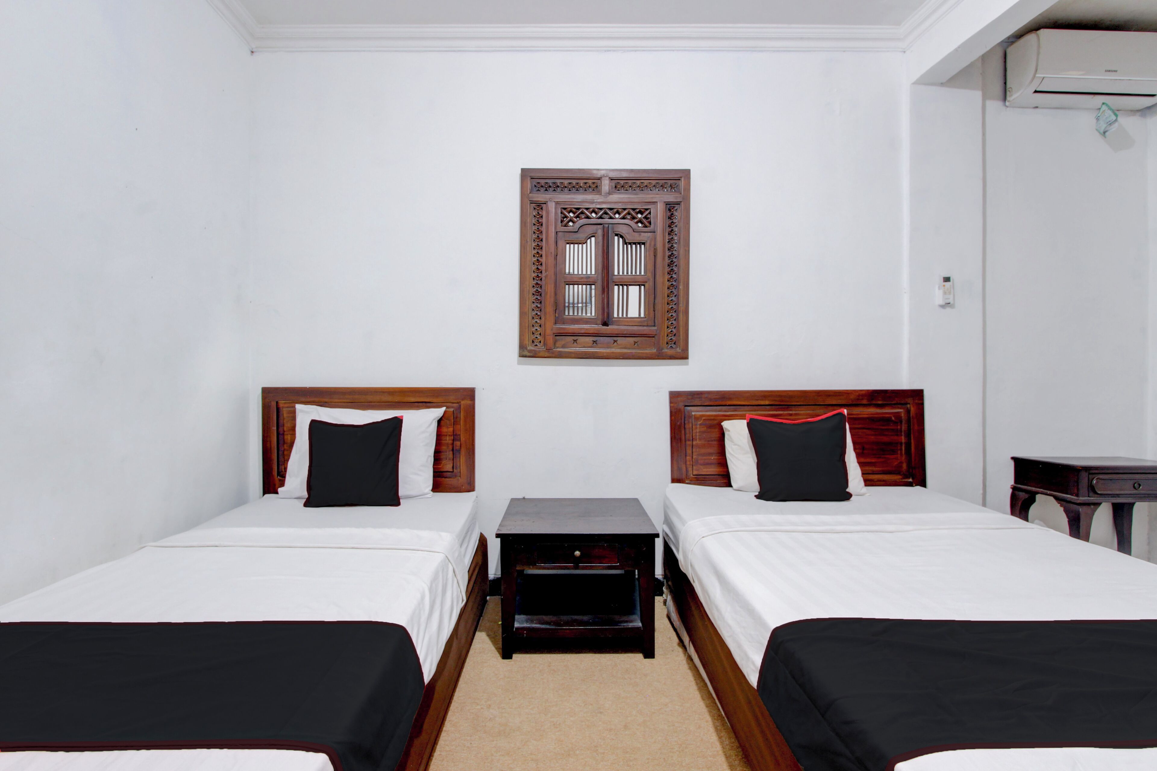A hotel room with two beds, a wooden headboard, a small table, and a wall-mounted air conditioning unit.
