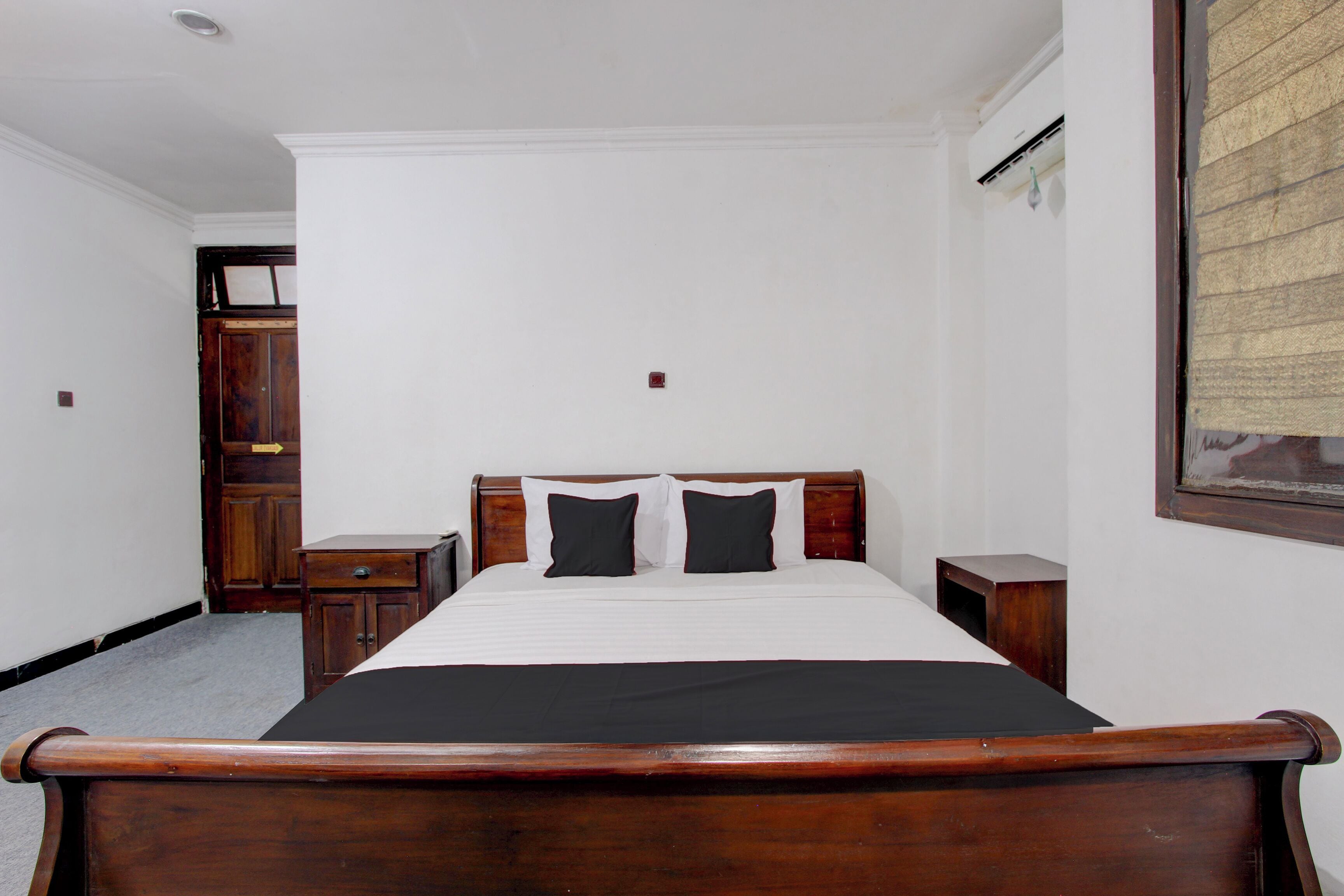 Un dormitorio con cama de madera, paredes blancas y mesita de noche de madera.