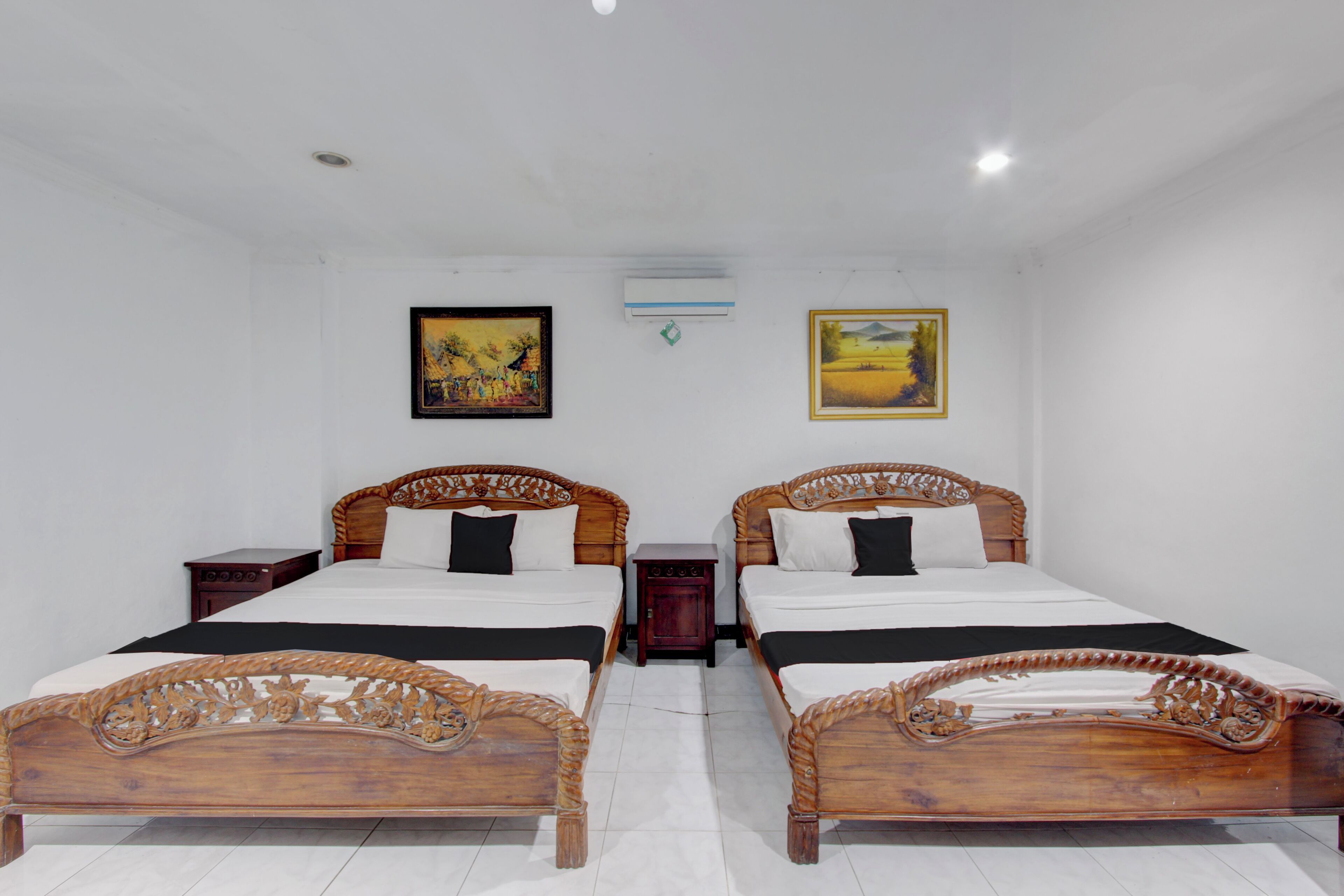 A room with two wooden beds, white walls, and two paintings.