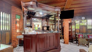 Un espace bar avec un comptoir en bois, des tabourets et un téléviseur fixé au mur.