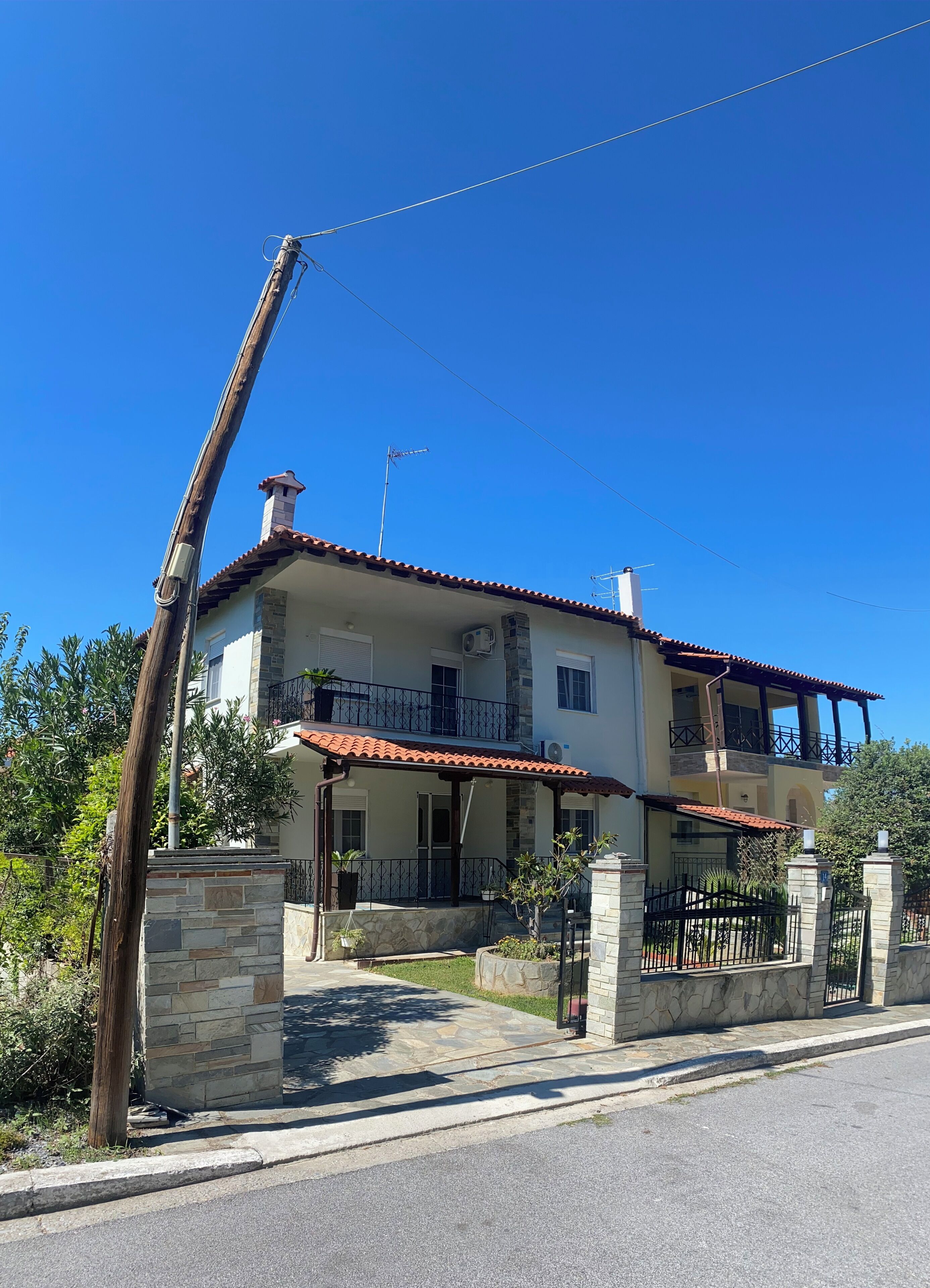 Une maison à deux étages, avec un toit recouvert de tuiles rouges, des piliers en pierre et un balcon.