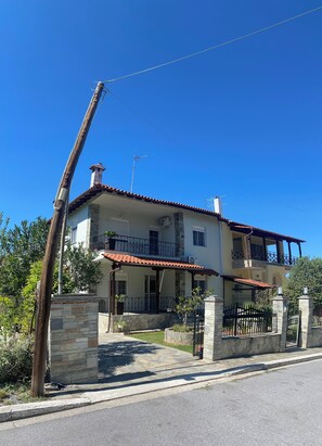A two-story house with a red-tiled roof, stone pillars, and a balcony.