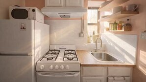 Cucina con piano cottura, forno a microonde, lavello e pensili bianchi.