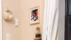 Una stanza con un tavolo di legno, una lampada, una radio, una pianta, un quadro incorniciato, un termostato e una tenda.