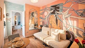 Un soggiorno con un divano, un tavolo da pranzo apparecchiato con piatti e posate, uno specchio e una parete decorata con un dipinto astratto.