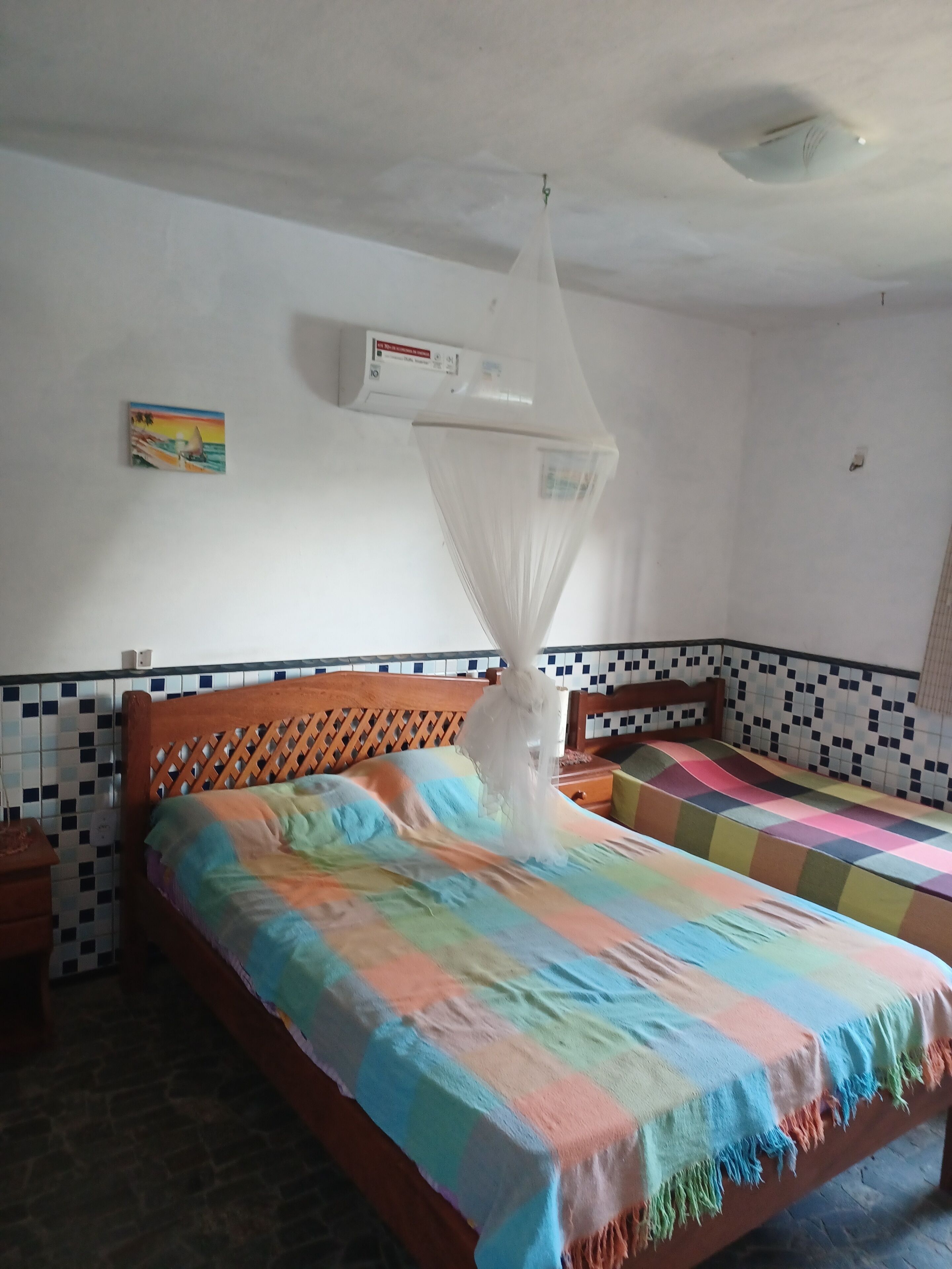 Quarto com cama, mesa de cabeceira, ar condicionado fixado na parede e parede revestida com azulejos.