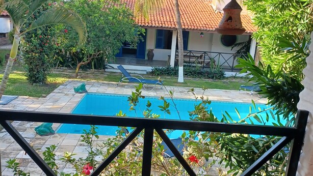 Un área de piscina con terraza de baldosas, una silla de descanso y un pequeño edificio con techo de tejas.
