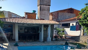 Una piscina con plataforma de baldosas, zona de bar y una chimenea alta.