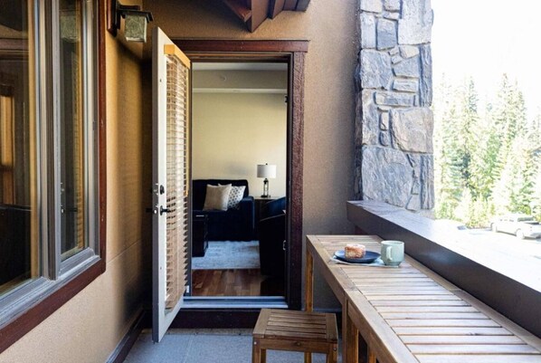 An open door leading to a bedroom with a bed, a nightstand, and a lamp. A wooden bench and a small table with a cup and a plate are outside the door. - Canmore Escape Creekside + Walk to Downtown (Canmore)