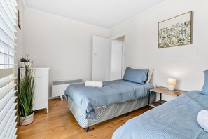 A bedroom with two beds, a radiator, a potted plant, and a framed picture on the wall.