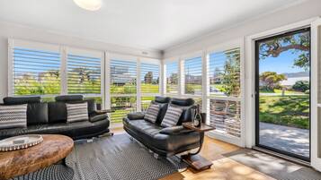 A spacious living area with a black leather sofa, a wooden coffee table, and a view of a green landscape through large windows.