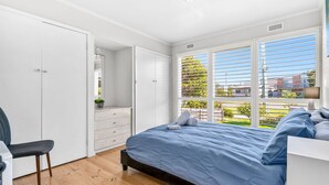 Een slaapkamer met een bed, een stoel, een dressoir en een raam met jaloezieën.