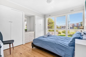 Ein Schlafzimmer mit einem Bett, einem Sessel, einer Kommode und einem Fenster mit Jalousien.
