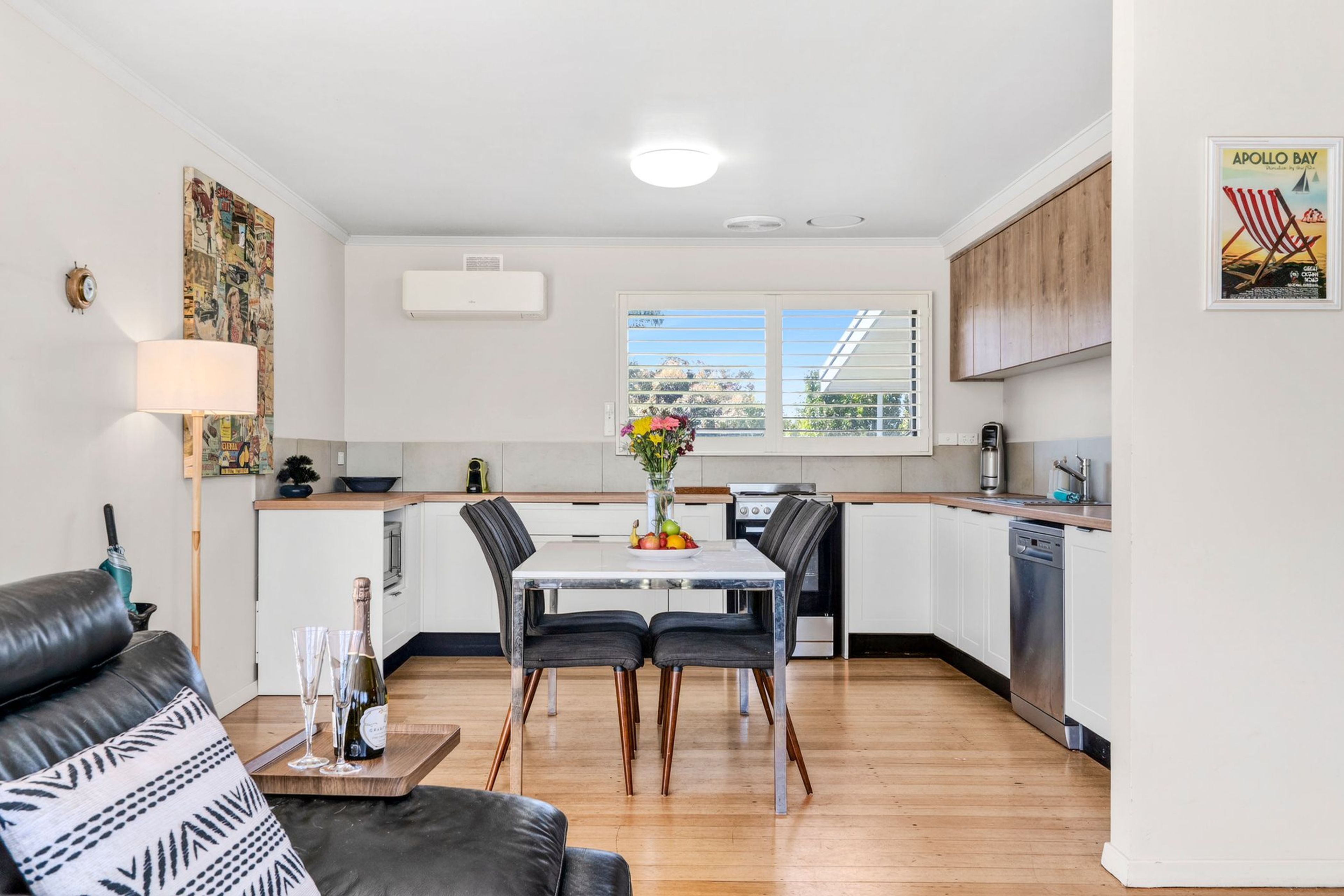 A compact kitchen with a dining area, featuring a table with chairs, a coffee machine, and a window with blinds.