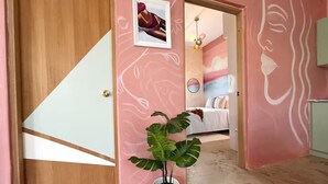 A hallway with a wooden door, a potted plant, and a bedroom with a bed and a wall painting. - Walk to Beach!「4 Bedroom」Vacation Home w Balcony! (Canals,)