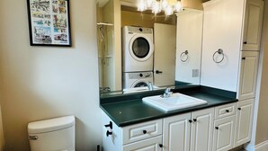A bathroom with a toilet, a sink, a mirror, a washing machine, and cabinets. - Mainfloor 3 bedroom, sleep 5-6, Kelowna wineries retreats (Kelowna)
