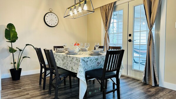 A dining area with a table set for four, chairs, a clock, and a potted plant.