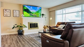 A living room with a fireplace, a television, leather sofas, and a large window.