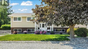 A two-story house with a front porch, a small garden with flowers, and a tree. - Mainfloor 3 bedroom, sleep 5-6, Kelowna wineries retreats (Kelowna)