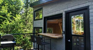 Una cabaña moderna con terraza, asientos integrados y amplios ventanales con vistas a un bosque.