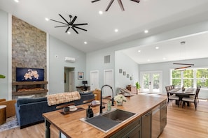 A spacious kitchen with a large island, a stone accent wall, and a dining area with a view. - Modern Retreat with Hot tub and Ensuite Bathrooms (Old Fort)