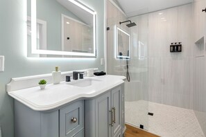 A bathroom with a double sink vanity, a large mirror with under-cabinet lighting, a shower enclosure, and a small plant on the vanity. - Fantastic 4-bedroom house with AC in charming Old Fort (Old Fort)