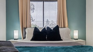 A neatly made bed with a teal blanket, two bedside lamps, and a window with curtains. - Great for Mid/Long Stays - Pool - King Bed (Mesa)