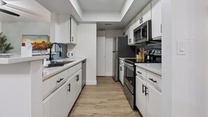 A modern kitchen with white cabinetry, a microwave, stove, and a sink. - Great for Mid/Long Stays - Pool - King Bed (Mesa)