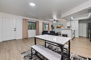 A modern kitchen with a refrigerator, a dining area with a table and bench, and a ceiling fan.