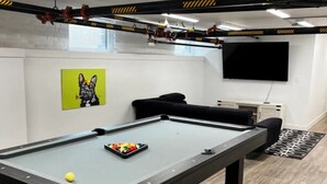 Un biliardo con le palle, un divano, un televisore e un quadro appeso al muro.